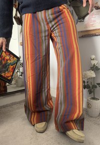 Wide-leg, striped trousers in red, orange, green, blue, and purple. Made from textured fabric. Features a relaxed fit and considerable length.