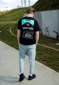 Juodas marškinėliai su turkio ir baltu grafiniu dizainu, pilkos sportinės kelnės ir juodi sportbačiai su raudonais akcentais. Matomi logotipo ir tekstiniai detalės.