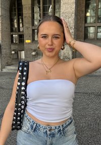 Top bianco senza spalline, pantaloni denim a vita alta e una borsa nera con borchie. Orecchini a cerchio dorati e collane dorate a strati.