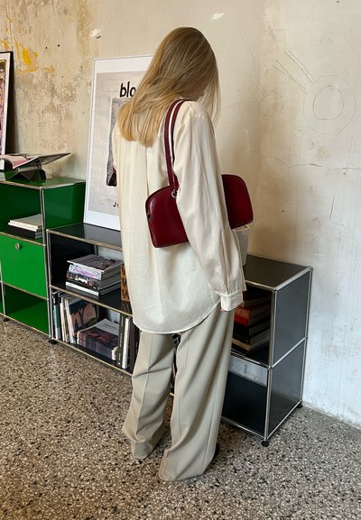 Camisa blanca de manga larga, de corte holgado, combinada con pantalones de pierna ancha de color beige claro. Bolso burdeos de forma curva con una correa de hombro.