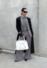 Sort uldfrakke, gråstribet blazer, grå skjorte og grå bukser med vide ben. Hvid håndtaske med sølvdetaljer, sorte solbriller og handsker.