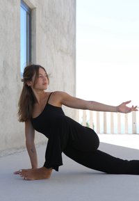 Black tank top and flared pants, person in a yoga pose on a smooth surface. Light background, natural light. Soft texture, relaxed posture.