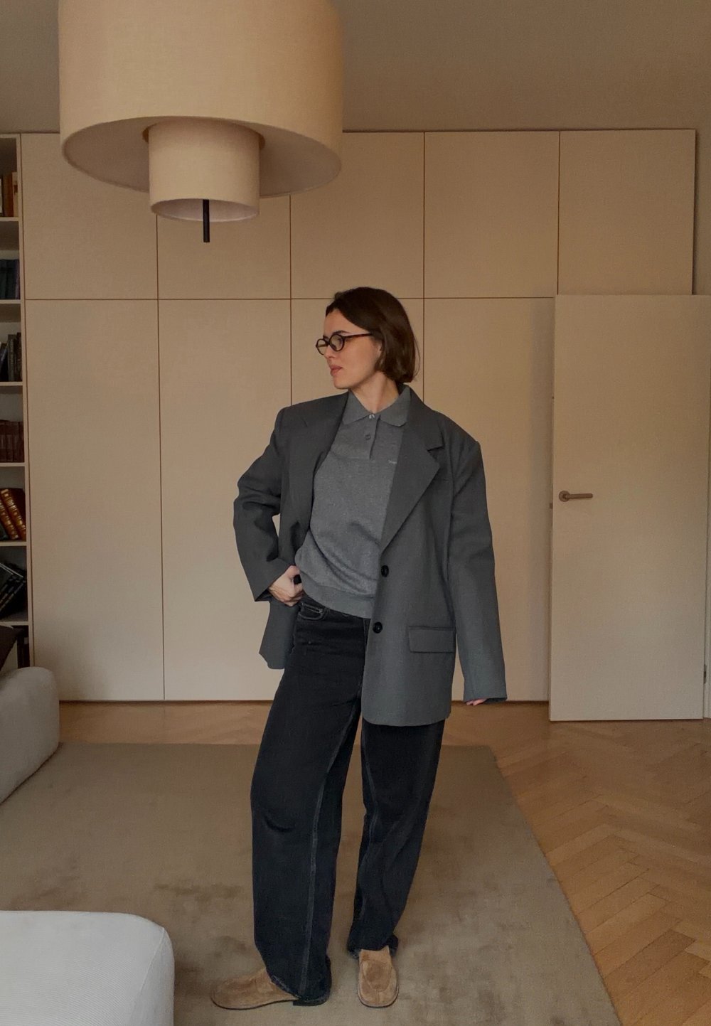 Veste blazer grise oversize avec pantalon noir et polo gris. Texture douce, design simple, palette de couleurs neutres, en intérieur.