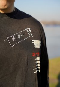 Schwarzes Langarm-T-Shirt mit weißen und roten Grafiken, darauf der Text "wow!!" und horizontale Streifen, aus Baumwolle oder ähnlichem Material gefertigt.