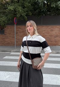 Polo a righe bianco e nero, maniche corte, abbinato a una gonna plissettata grigio scuro. Borsa a tracolla marrone con motivo logo.