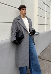 Sobretudo cinzento com padrão espinha de peixe e grandes lapelas, usado por cima de uma t-shirt branca. Combina com jeans azuis largos e uma mala preta de couro. Luvas pretas.