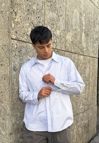 Svijetloplava i bijela prugasta košulja s dugim rukavima i opuštenim krojem. Ima mekanu teksturu i dugih rukava s dugmadi na manžetama.