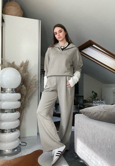 Sudadera gris claro con capucha y puños de punto blancos, combinada con pantalones de pierna ancha gris claro a juego. Zapatillas negras y blancas.