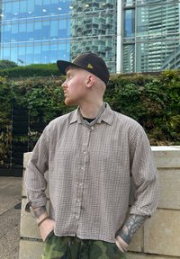 Pruuni ja valge ruuduline särk, kerge kangas, kantud musta mütsi ja kettkaelakeega, kombineeritud kamuflaažimustriga pükstega.