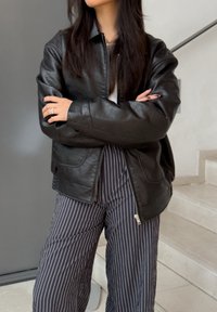 Svart läderjacka med dragkedja, ribbat mönster och sidofickor. Matchad med marinblå randiga vida byxor.