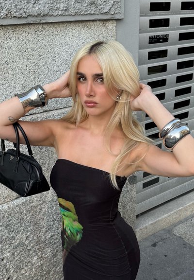Vestido negro sin mangas con un estampado de pájaros coloridos, brazalete plateado en un brazo y un pequeño bolso negro. Fondo texturizado.