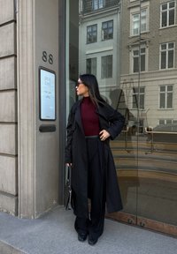 Must mustrükk ümber burgundia värvi poolkaelusega sviitri, koos laiade mustade pükstega. Aksessuaarideks on tumedad päikeseprillid ja väike must kott.
