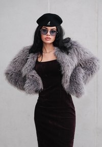 Szara, puszysta kurtka futrzana o szerokich rękawach na dopasowanej, ciemnoczerwonej burgundowej sukience. Czarny beret i oversize'owe okulary przeciwsłoneczne dopełniają look.