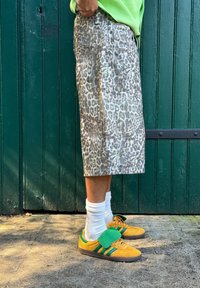 Σορτς από ύφασμα με λεοπάρ μοτίβο και άνετη εφαρμογή, σε γκρι και μπεζ χρωματική παλέτα, συνδυασμένα με κίτρινες και πράσινες αθλητικές κάλτσες και λευκές κάλτσες.