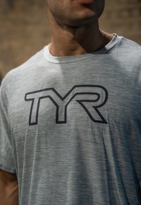 Himmelblaues Trainings-T-Shirt aus feuchtigkeitsableitendem Material, mit einem dunkelblauen "TYR"-Logo, das zentral auf der Brust platziert ist.