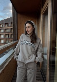Ensemble sweat à capuche beige et pantalon de survêtement avec logo "LAMANIA". Tissu doux, coupe décontractée et capuche. Conçu pour le confort et un style décontracté.