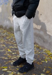 Calças de moletão cinzentas com punhos elásticos, combinadas com sapatilhas de atletismo pretas, colocadas contra um pano de fundo de folhas caídas sobre um pavimento.