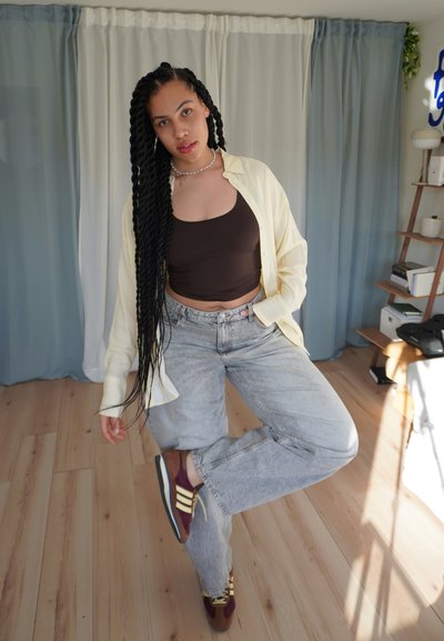Conjunto informal que incluye una camiseta de rayas amarillas y blancas, un top corto marrón, jeans de lavado claro y zapatillas deportivas burdeos con acentos amarillos.