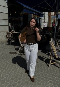 Bruine korte mouw gebreide top, witte wijde broek, bruine suède tas en bruine schoenen. Buitencafé met stenen bestrating en meubels.