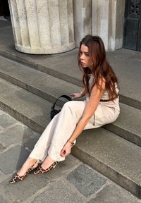 Combinaison sans manches beige avec une coupe ample, associée à des talons slingback à bout pointu ornés d'un imprimé léopard. Un sac à main noir est posé à côté.