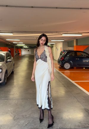 Vestido de satén blanco con ribete de encaje negro, que presenta un escote en V profundo y una abertura lateral. Se lleva con un accesorio blanco esponjoso y tacones negros.