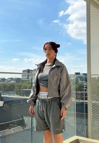 Lichtgrijze cropped jack met ballonmouwen, gecombineerd met grijze shorts met trekkoord. Grijze tanktop eronder, zichtbaar Calvin Klein tailleband.