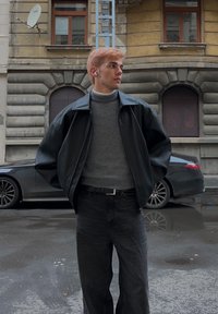 Sort læderjakke over en grå rullekrave, kombineret med mørke jeans. Baggrunden viser en bygning og en bil.