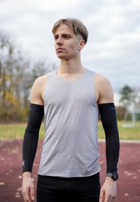 Halli varrukateta sportlik särk, mida on kantud koos mustade pika varrukaga aluspesuga. Disain on keha järgi lõigatud ja näitab sujuvat tekstuuri. Randmel on must käekell.