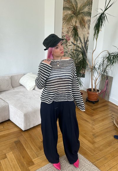 Suéter de punto a rayas blancas y negras con un diseño de hombro descubierto, combinado con pantalones holgados negros y zapatos de punta rosa brillante. Sombrero incluido.