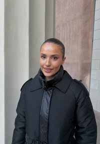 Czarna pikowana kurtka z wysokim kołnierzem, łącząca matowe i błyszczące faktury, z bocznymi kieszeniami i paskiem w talii.