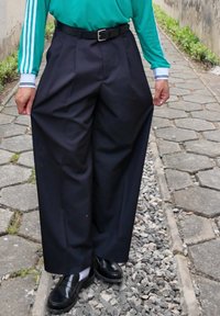 Pantalon noir à jambes larges avec une taille haute, accompagné d'une ceinture noire. Le tissu semble lisse avec une légère brillance. Porté avec des chaussures noires brillantes.