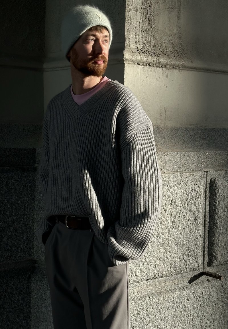 Pull gris surdimensionné à côtes avec un col en V et des manches longues, associé à un pantalon gris clair et un bonnet doux bleu clair.