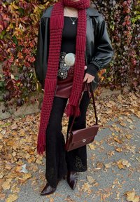 Červený pletený šátek, černá kožená oversize bunda, přiléhavé černé krajkové kalhoty s rozšířenými nohavicemi, pásek se stříbrnými detaily a vínová kabelka s klopou.