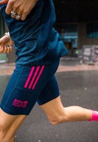 Futó sötétkék BMW Berlin Maraton rövidnadrágban, rózsaszín csíkkal és felirattal, fényképezve futás közben egy városi utcán.