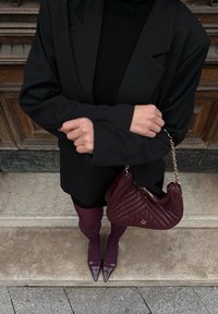 Black oversized blazer over a black roll-neck jumper, paired with a burgundy handbag featuring a quilted design, matching tights, and pointed-toe heels.