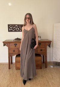 Robe maxi marron fluide avec fines bretelles spaghetti ; assortie à un petit sac à main noir et des talons pointus noirs ; design minimaliste.