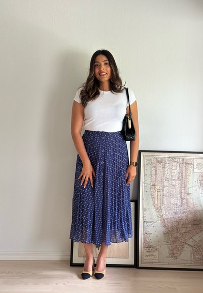 Una camiseta blanca ajustada combinada con una falda midi plisada azul marino con lunares blancos. Un bolso negro y unos zapatos bicolores completan el look.