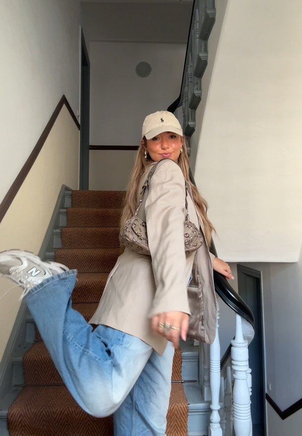 Mujer con ropa informal y gorra posa juguetonamente en la escalera, levantando una pierna mientras sostiene la barandilla.