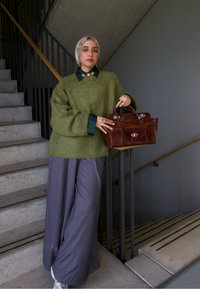 Zelený pletený oversized svetr, nošený přes košili s límečkem, doplněný širokými šedými kalhotami. Drží hnědou koženou kabelku, stojí na schodech.