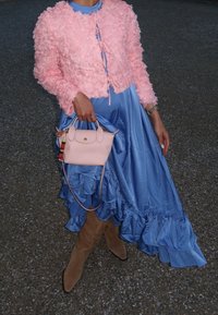 Ροζ σακάκι με λουλουδάτη υφή, μπλε σατέν φόρεμα με ρυάκι στο τελείωμα, μπεζ μπότες μέχρι το γόνατο και μια μικρή ροζ τσάντα χειρός με πολύχρωμο γούρι.