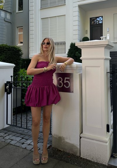 Vestido sin tirantes fucsia con un corsé fruncido y falda acampanada. Combinado con tacones de plataforma en tonos neutros y varias pulseras de oro.