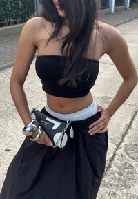 Top cropped preto, saia branca de cintura alta e bolsa com corrente de bolinhas brancas e pretas. Uma pulseira prateada no pulso acrescenta brilho.
