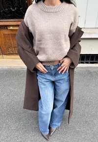 Beežist kudumiga kampsun ribaga kaelusega, pruun oversize mantel, kõrge vöökohaga helesinised teksad ja pruunid terava ninaga kontsakingad.