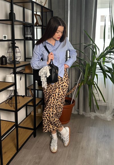 Camisa de rayas azul claro con mangas largas, falda de estampado de leopardo, zapatillas blancas con acentos grises, sosteniendo un bolso negro con detalle de encaje.