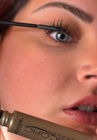 Musta ripsiväritela levittää tuotetta pitkille ripsille. Tuubissa on beige pohja mustilla kirjaimilla. Iho on sileä ja luonnollinen.