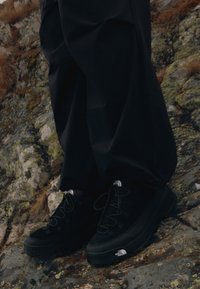 Μαύρα παπούτσια πεζοπορίας με υφασμάτινη σουέτ επιφάνεια, με ενισχυμένο κάλυμμ�α δαχτύλων και λογότυπο στο πλάι. Φοριούνται σε βραχώδη έδαφος.