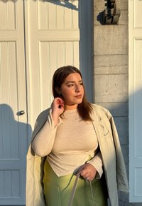 Lys beige langærmet top parret med en oversized cremefarvet blazer og en svævende lys grøn nederdel. Holder en lys handbag.