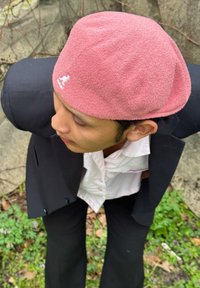 Pink textured cap worn with a black suit, featuring a kangaroo logo. The background includes greenery and stone elements.