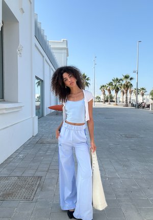 Top ajustado de color azul claro combinado con pantalones anchos de pierna suelta en tono azul pálido con rayas laterales. Un cárdigan corto blanco y un bolso blanco complementan el look.