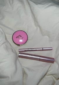 Te chique roze compact van Too Faced met spiegel, twee roze mascara's met zwarte tekst "Better Than Sex," op een lichte stoffen achtergrond.